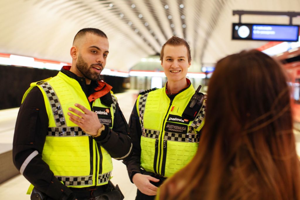 Palmian järjestyksenvalvojat juttelevat asiakkaalle metroasemalla